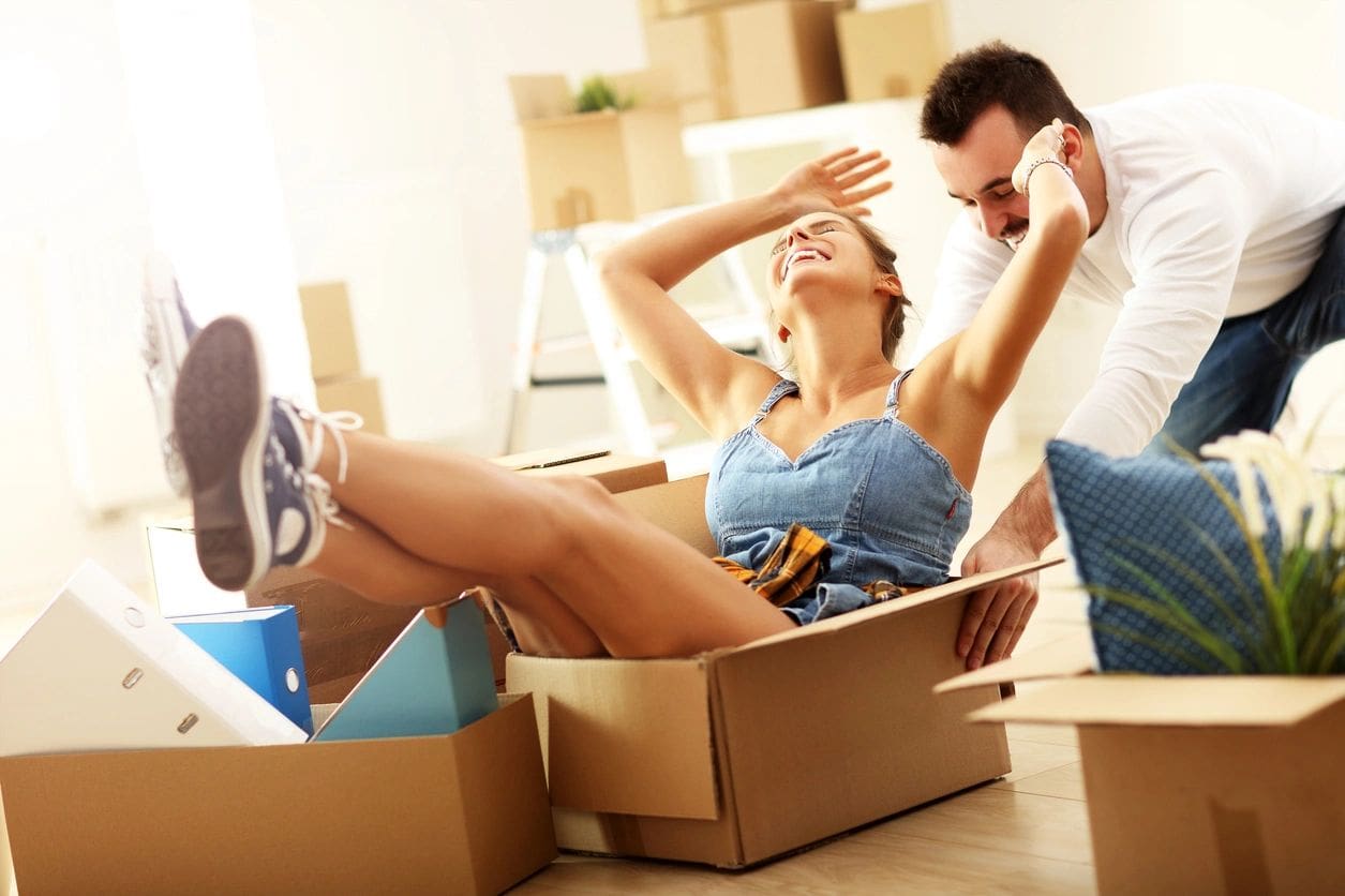 A woman laying in the middle of a box while another man sits on her lap.