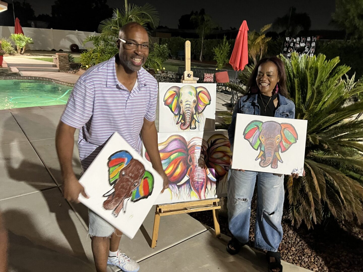 Two people holding up paintings of elephants.