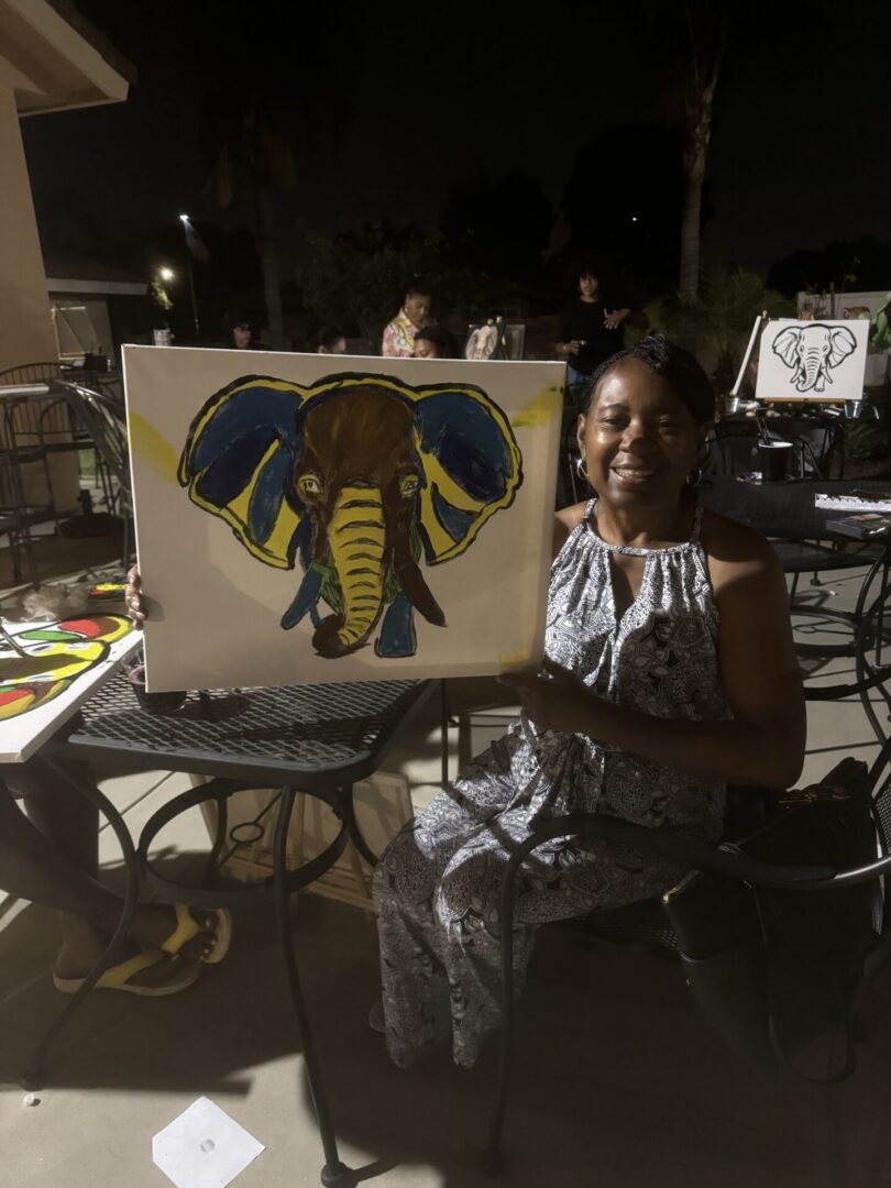 A woman sitting in front of an elephant painting.