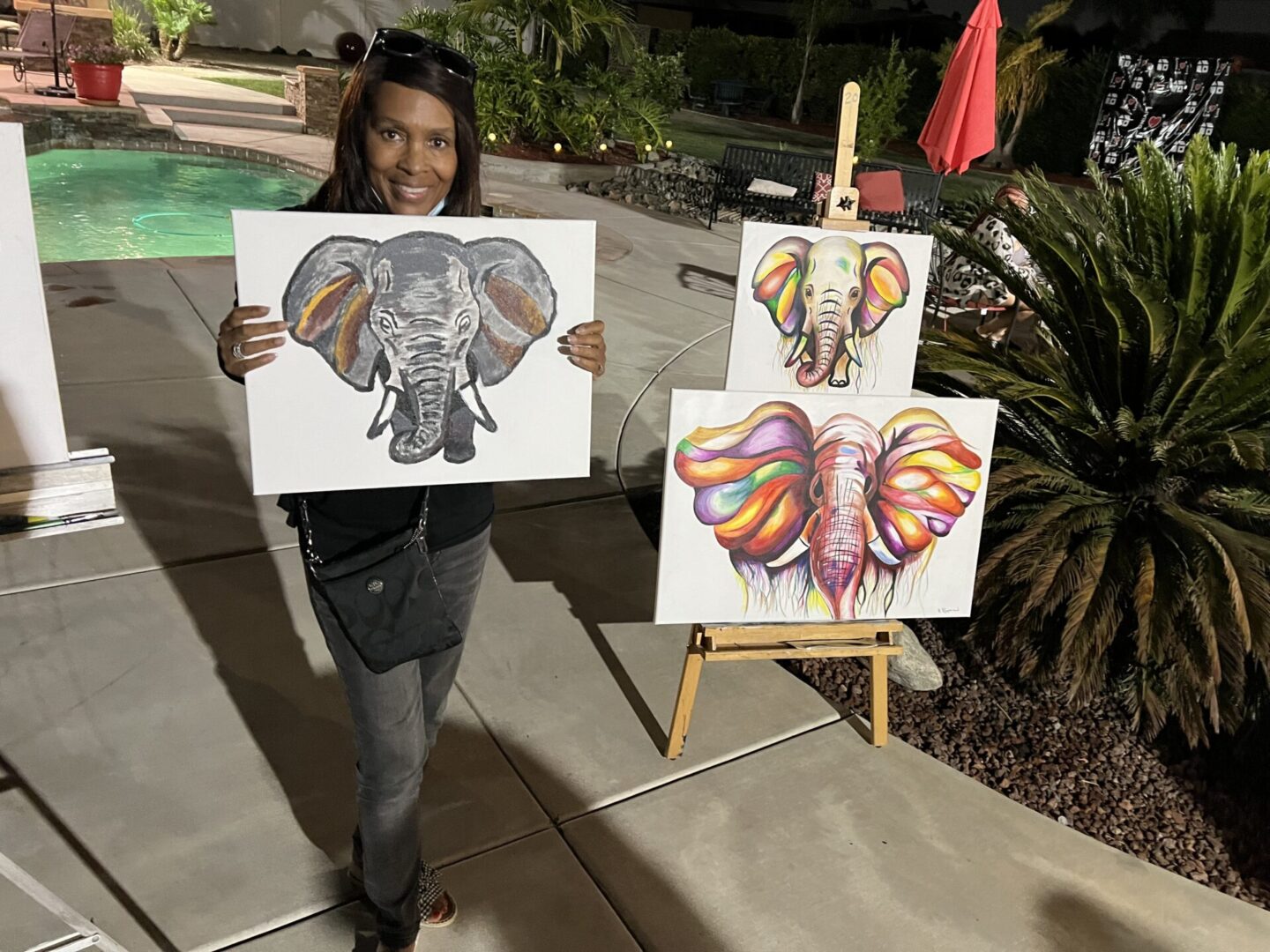 A woman holding two paintings of elephants.