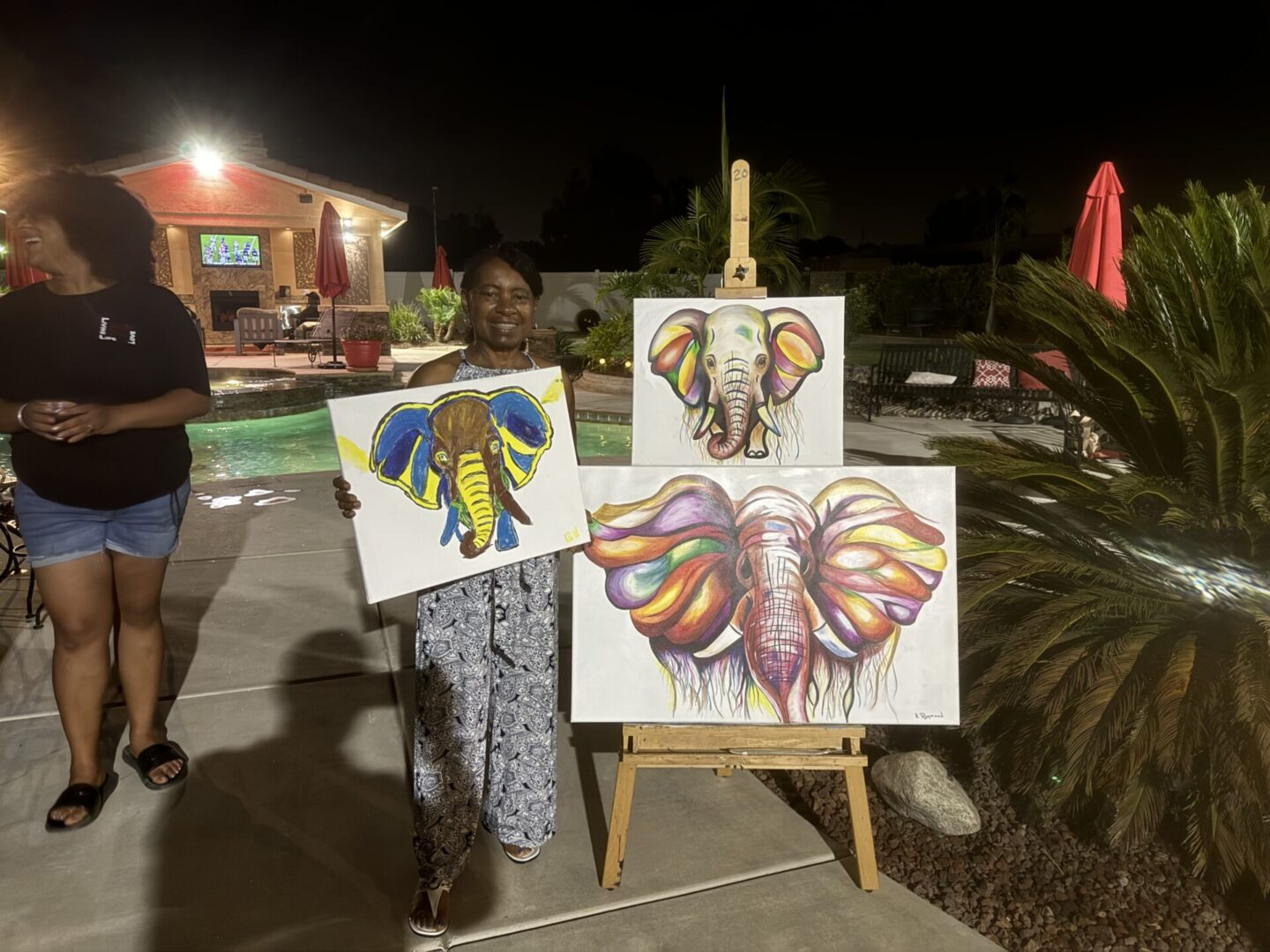 A woman holding two paintings of elephants on canvas.