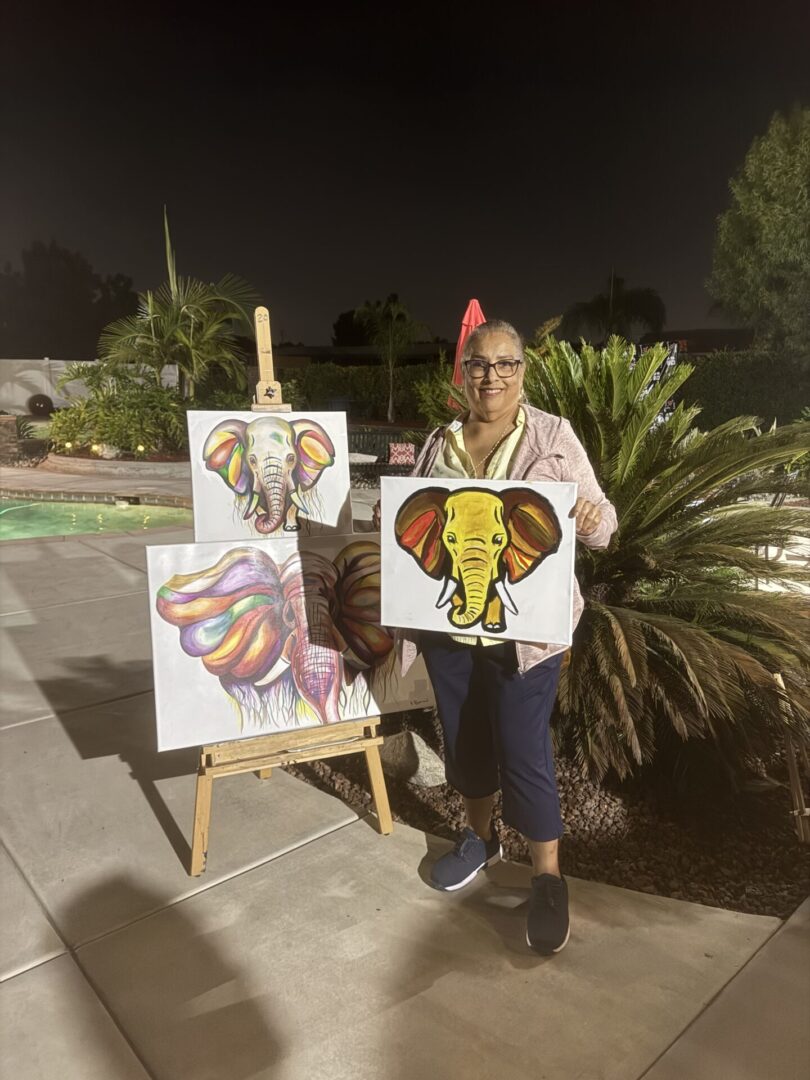 A woman holding up two paintings of elephants.