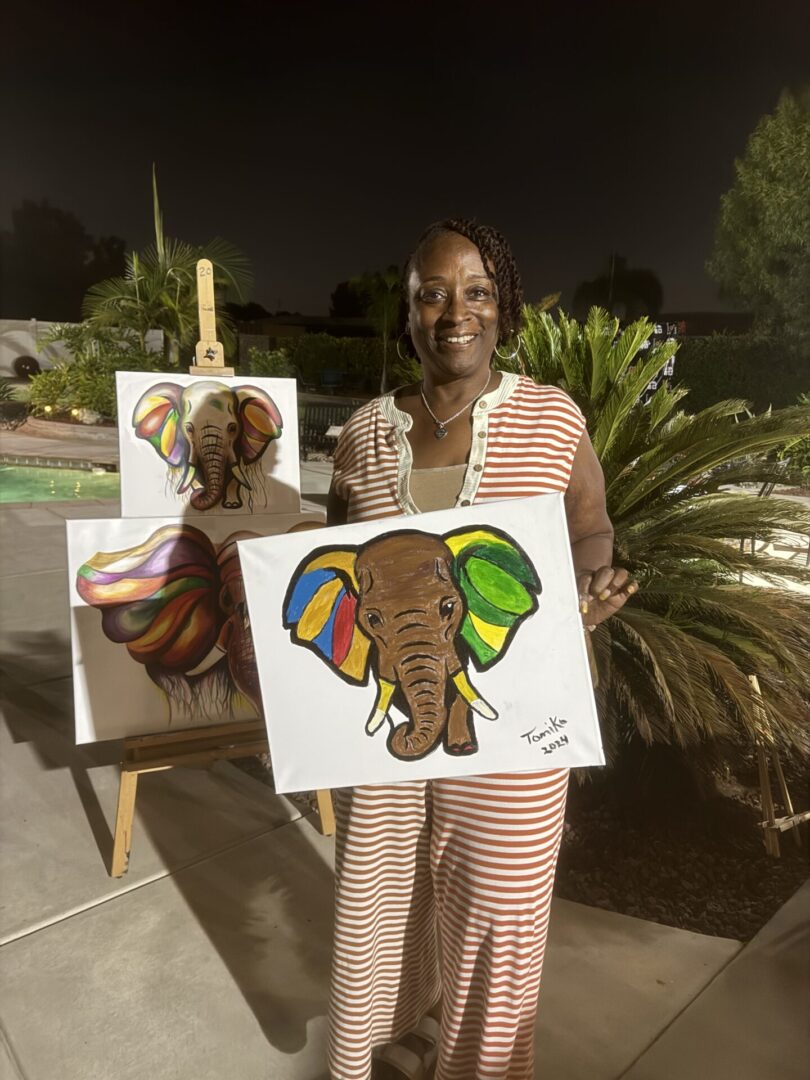 A woman holding an elephant painting in front of two other people.