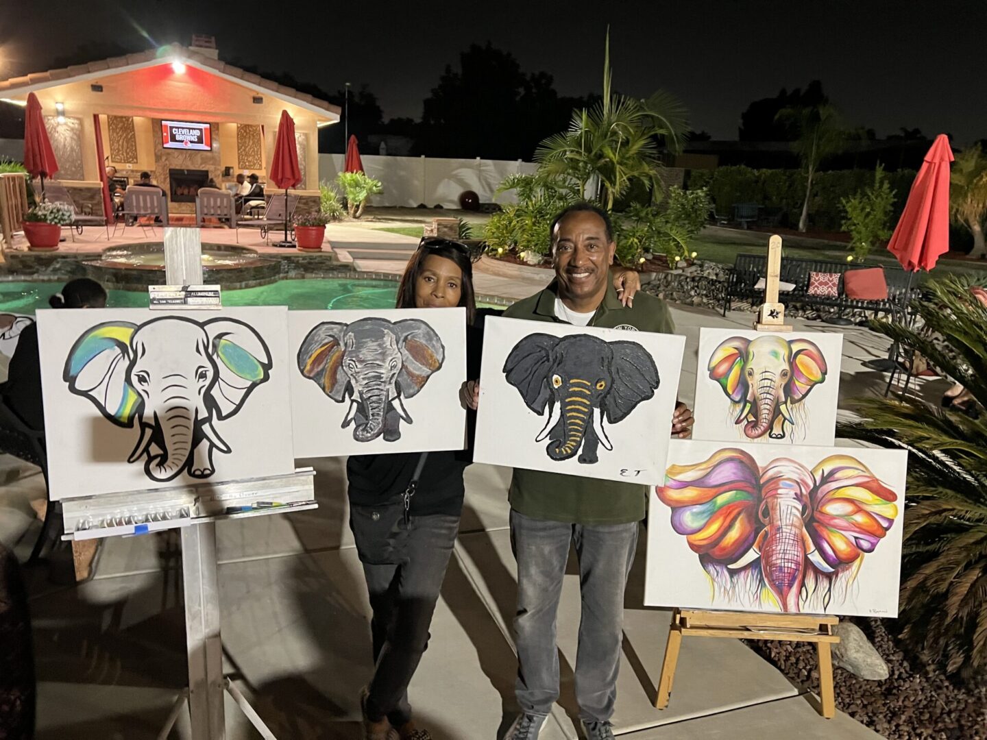 Two people holding up paintings of elephants.