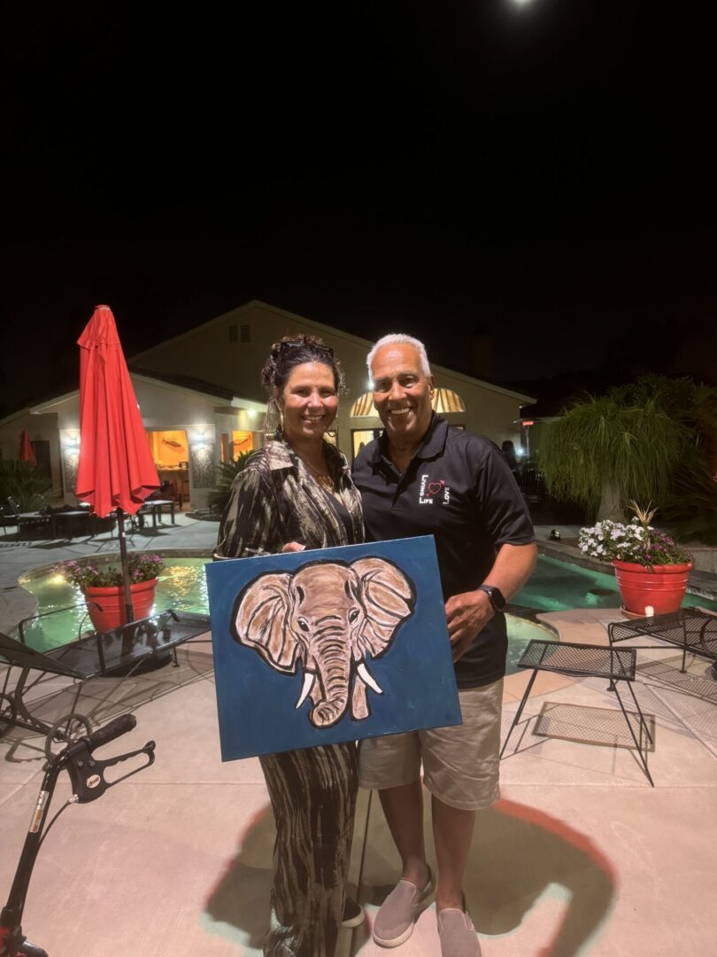 A man and woman holding an elephant painting.